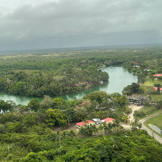 Aerial view in Belize of a river surrounded by lush greenery and small buildings.