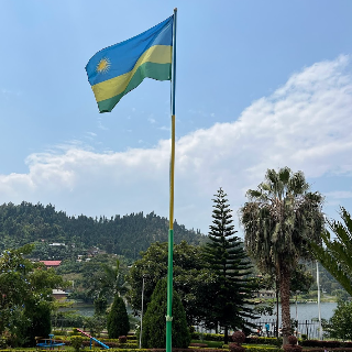 Flag of Rwanda waving in front of a scenic landscape with trees and a lake
