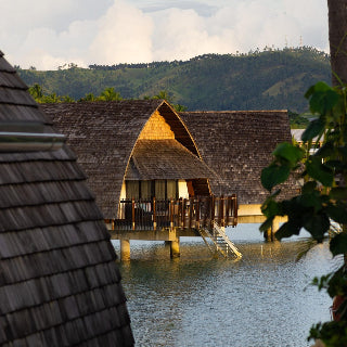 Wooden overwater bungalows with thatched roofs in a tropical setting.